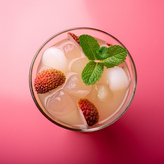 Top view of lychee mojito with ice cubes, fresh lychee fruit, nata de coco, and mint leaves in a glass on a pink background.