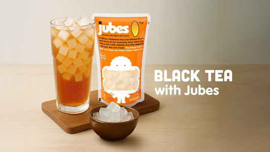 Glass of iced black tea with coconut jelly cubes beside an orange Jubes pack and a small bowl of jelly cubes, with text that reads 'Black Tea with Jubes'.