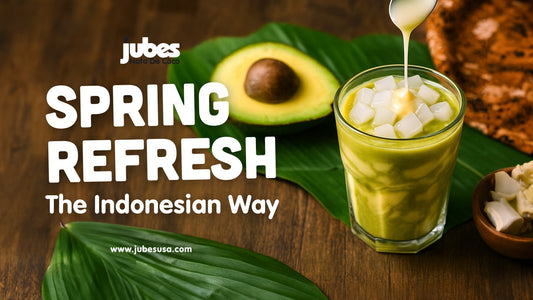 Glass of green Es Alpukat avocado dessert topped with coconut jelly cubes and condensed milk drizzle, placed beside a halved avocado and tropical leaves, with text that reads 'Spring Refresh – The Indonesian Way'.