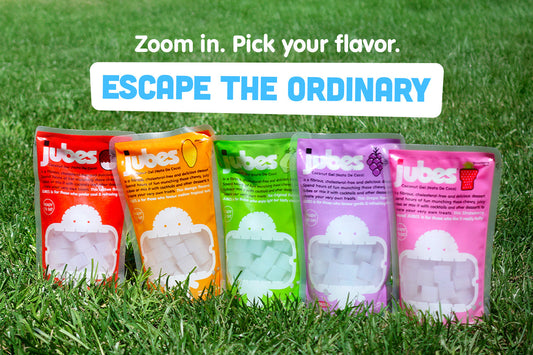 Five Jubes nata de coco pouches in Original, Mango, Lychee, Grape, and Strawberry flavors displayed on green grass.