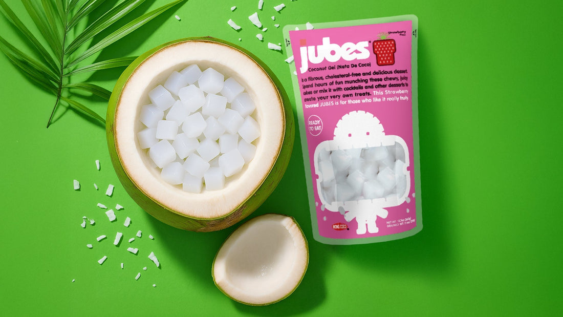 Strawberry Jubes nata de coco pouch with fresh coconut cubes in a shell on a green background.