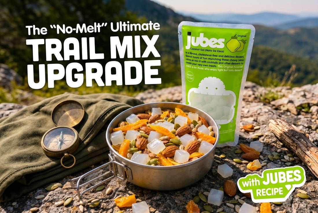 Metal camp bowl of trail mix with almonds, dried mango, and Jubes Original coconut jelly cubes, beside a compass on a rocky overlook.