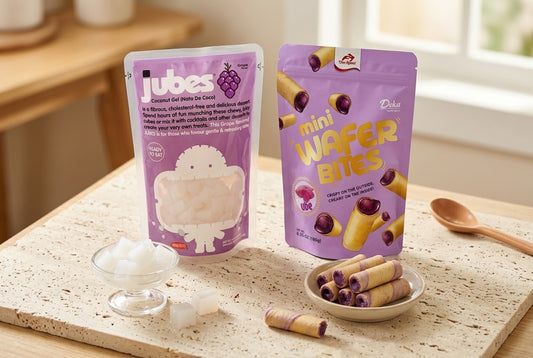 A Jubes Grape coconut jelly pouch next to a Deka Ube Mini Wafer Bites pouch, with loose coconut cubes and wafer rolls in small dishes.