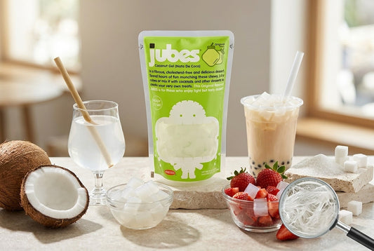 A bag of Jubes Original Nata De Coco beside a bowl of coconut jelly cubes, a coconut, strawberries, and a boba milk tea.