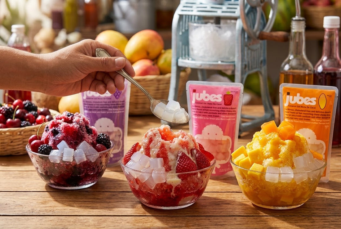 A hand spoons Jubes nata de coco over bowls of berry, strawberry, and mango shaved ice beside Jubes pouches and a hand-crank ice shaver.