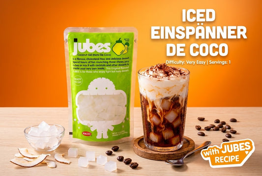 A green Jubes Original pouch beside an iced Einspanner coffee topped with whipped cream, coconut jelly cubes, and scattered coffee beans.