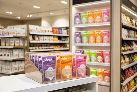 A cardboard countertop display and full store shelf stocked with Jubes coconut jelly pouches in grape, lychee, mango, and strawberry.