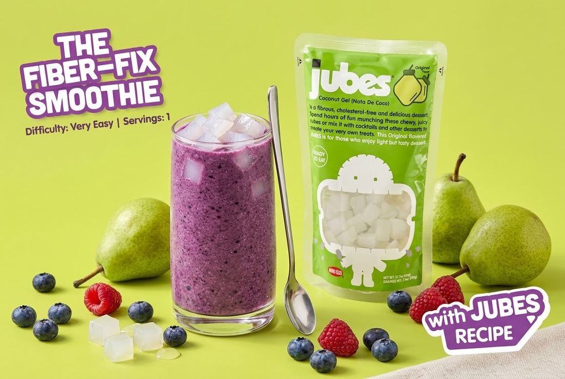 A purple blueberry spinach smoothie topped with coconut jelly cubes beside a Jubes Original pouch, pears, blueberries, and raspberries.