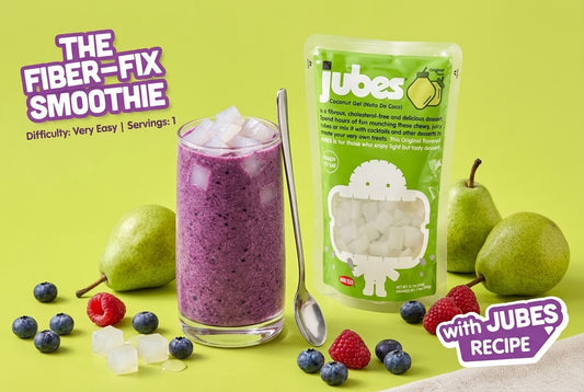 A purple blueberry spinach smoothie topped with coconut jelly cubes beside a Jubes Original pouch, pears, blueberries, and raspberries.