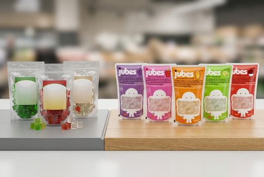Split comparison of plain unbranded coconut jelly pouches beside five branded Jubes pouches in various flavors on a counter.