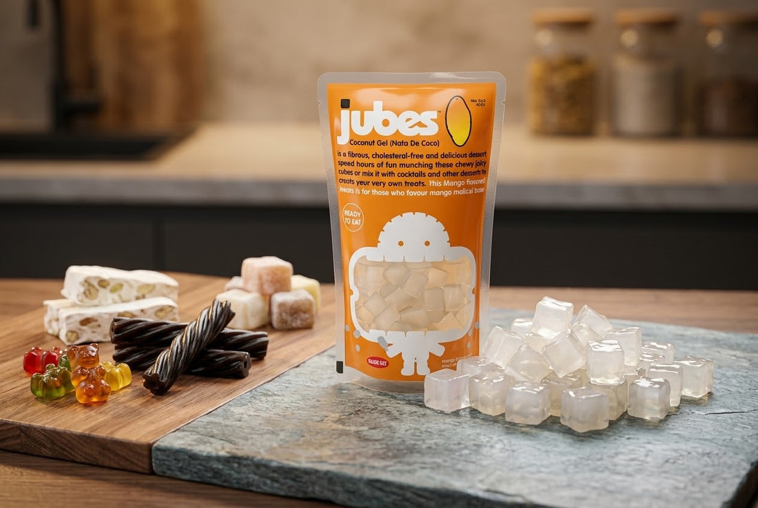 A Jubes Mango coconut jelly pouch on a counter next to nougat, gummy bears, licorice twists, and a pile of loose coconut jelly cubes.
