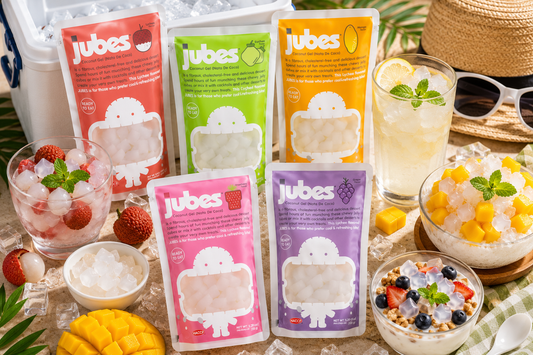 Jubes Nata De Coco pouches surrounded by chilled coconut jelly cubes, tropical fruits, iced drinks, and summer desserts on a bright tabletop.
