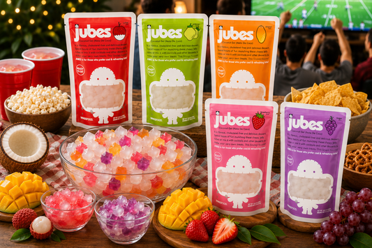 Jubes nata de coco coconut jelly pouches and mixed jelly cubes served in bowls on a snack table during a lively watch party with fruits, chips, and a football game in the background.