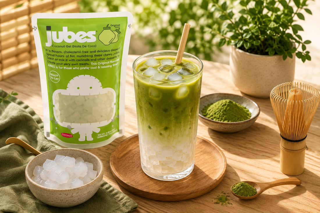 Iced matcha latte with chewy lychee nata de coco jelly cubes beside colorful Jubes pouches on a sunlit wooden table with tropical café styling.