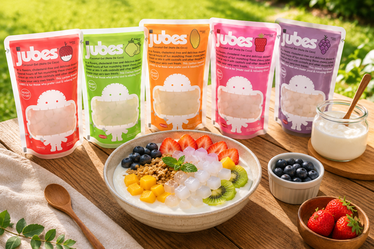 Creamy yogurt bowl topped with fresh berries, granola, and chewy nata de coco jelly cubes beside colorful Jubes pouches on a sunlit wooden table.