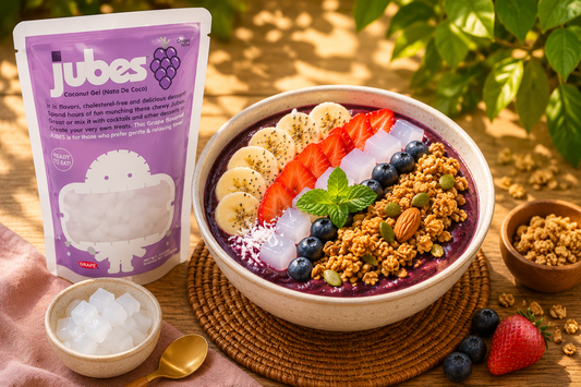 Acai bowl topped with fresh berries, kiwi, granola, and chewy nata de coco jelly cubes beside colorful Jubes coconut gel pouches on a tropical sunlit table.