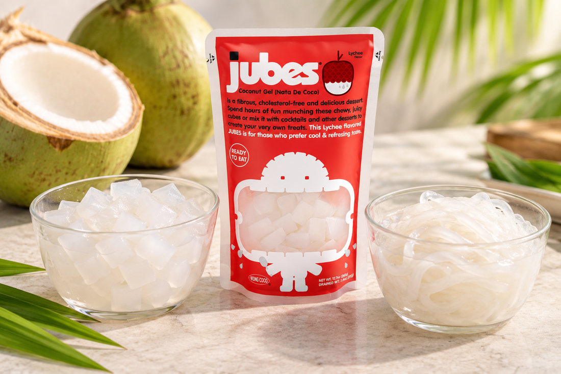 Jubes Lychee coconut gel pouch between a bowl of nata de coco cubes and a bowl of stringy coconut, with fresh coconuts and palm leaves.