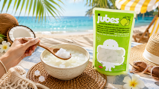 A bright lime-green pouch of Jubes Original Flavor Coconut Gel next to a ceramic bowl filled with translucent jelly cubes in coconut milk, set against a sunny tropical beach background.