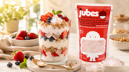A layered fruit and yogurt parfait with jelly cubes next to a red pouch of Jubes Coconut Gel