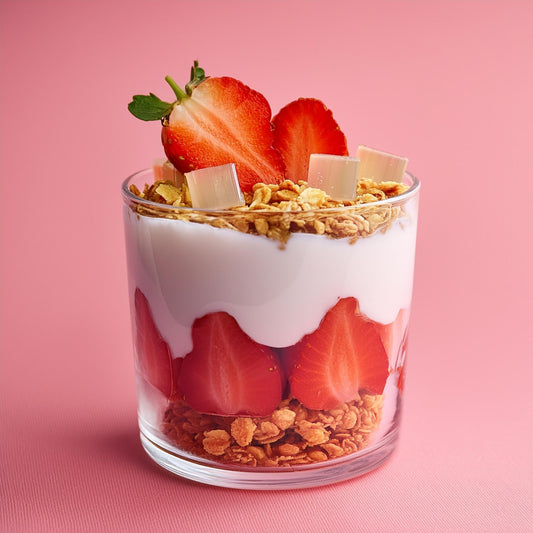 Glass of yogurt parfait layered with strawberries, granola, and coconut jelly cubes against a pink background.