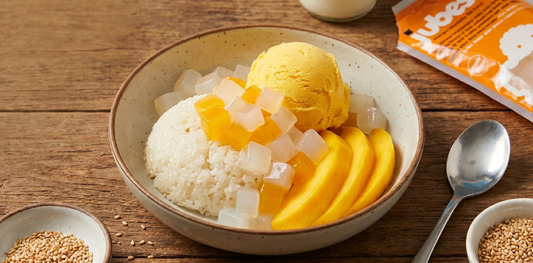 Thai mango sticky rice dessert served in a shallow ceramic bowl on a rustic wooden table.