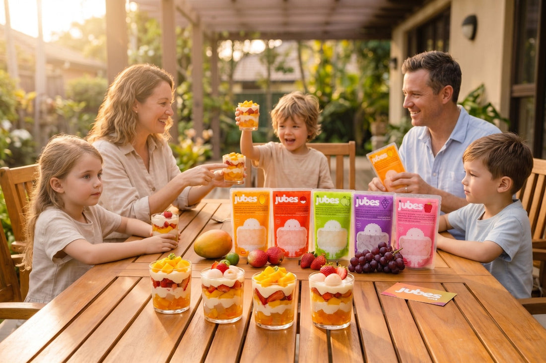 A happy family of five sits around an outdoor wooden table at sunset, enjoying fruit parfaits made with Jubes Nata De Coco pouches displayed in the center.