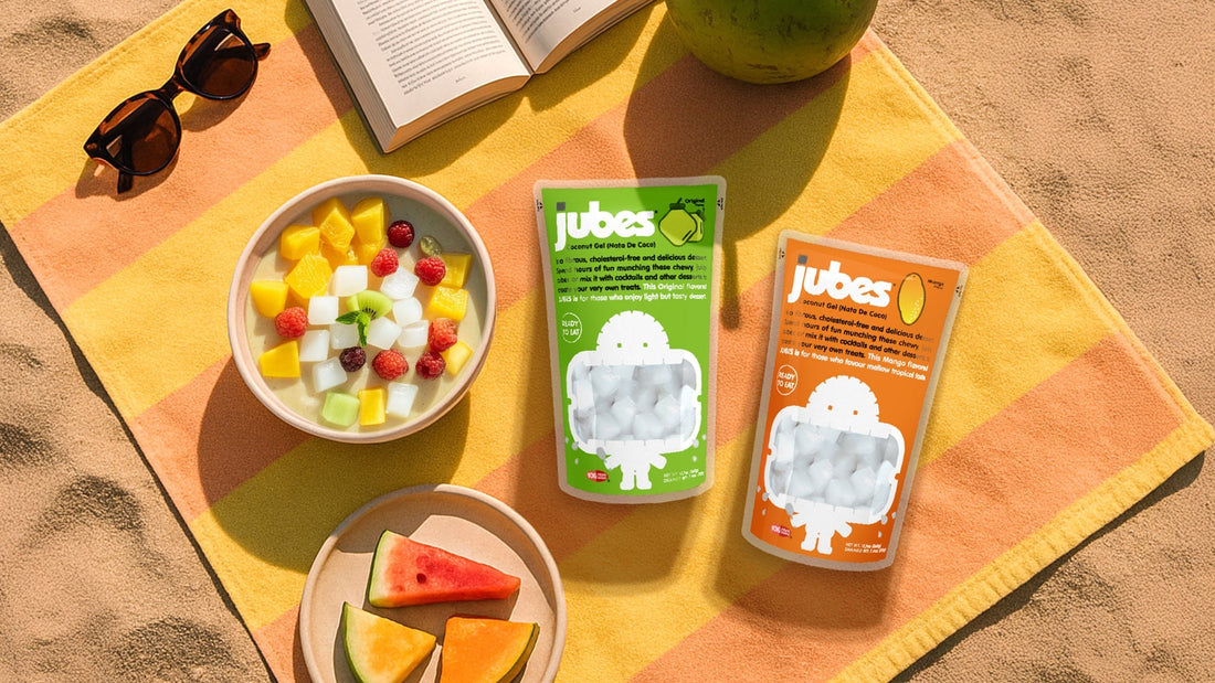 Picnic setup with fruit salad, watermelon, and Jubes nata de coco pouches in Lychee and Mango flavors on a blanket.