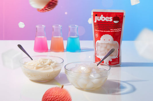 Jubes Lychee pouch beside dessert bowls with nata de coco and colorful beakers in the background.