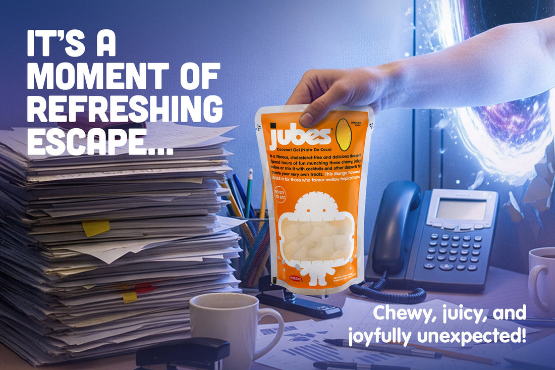 Hand grabbing a pouch of Jubes Mango Delights from a desk cluttered with paperwork, coffee, and office supplies.