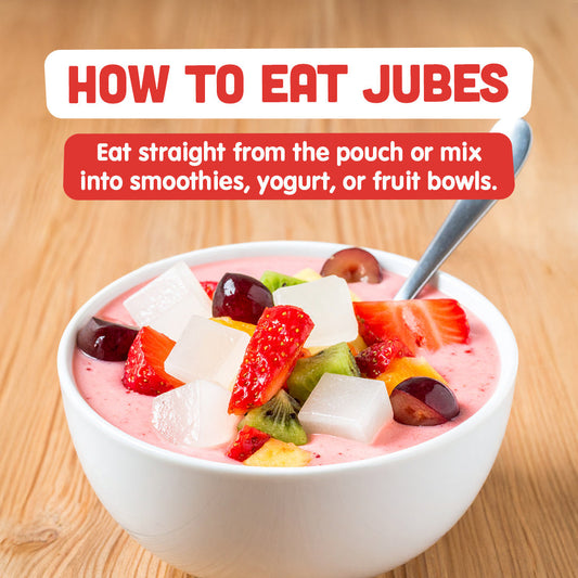White bowl of yogurt topped with Jubes coconut gel cubes, strawberries, grapes, and kiwi with text 'How to Eat Jubes'.