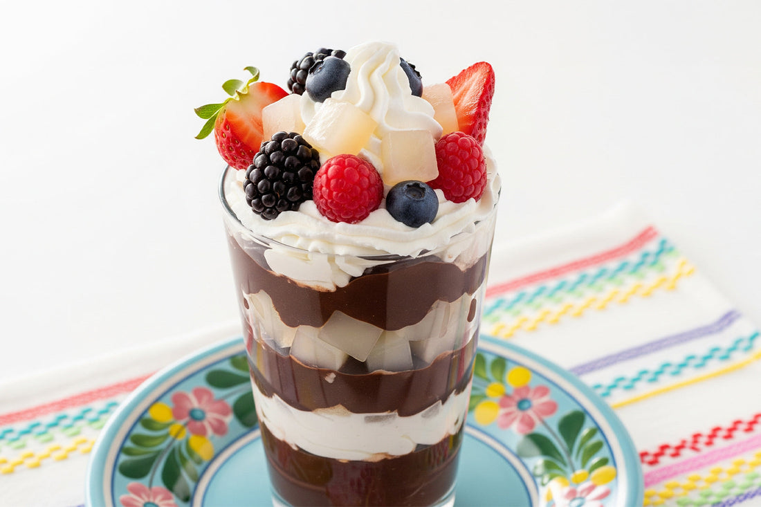Layered parfait glass filled with chocolate pudding, whipped cream, and coconut jelly cubes, topped with strawberries, raspberries, blackberries, blueberries, and whipped cream.