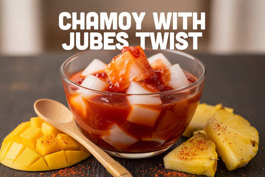 Glass bowl filled with coconut jelly cubes topped with chamoy sauce, placed beside slices of mango and pineapple with a wooden spoon, with text that reads 'Chamoy with Jubes Twist'.