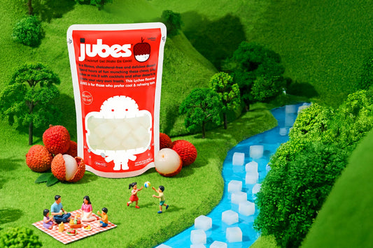 Jubes lychee nata de coco pouch displayed in a miniature picnic scene with lychee fruit, tiny figurines, and a river filled with coconut gel cubes.