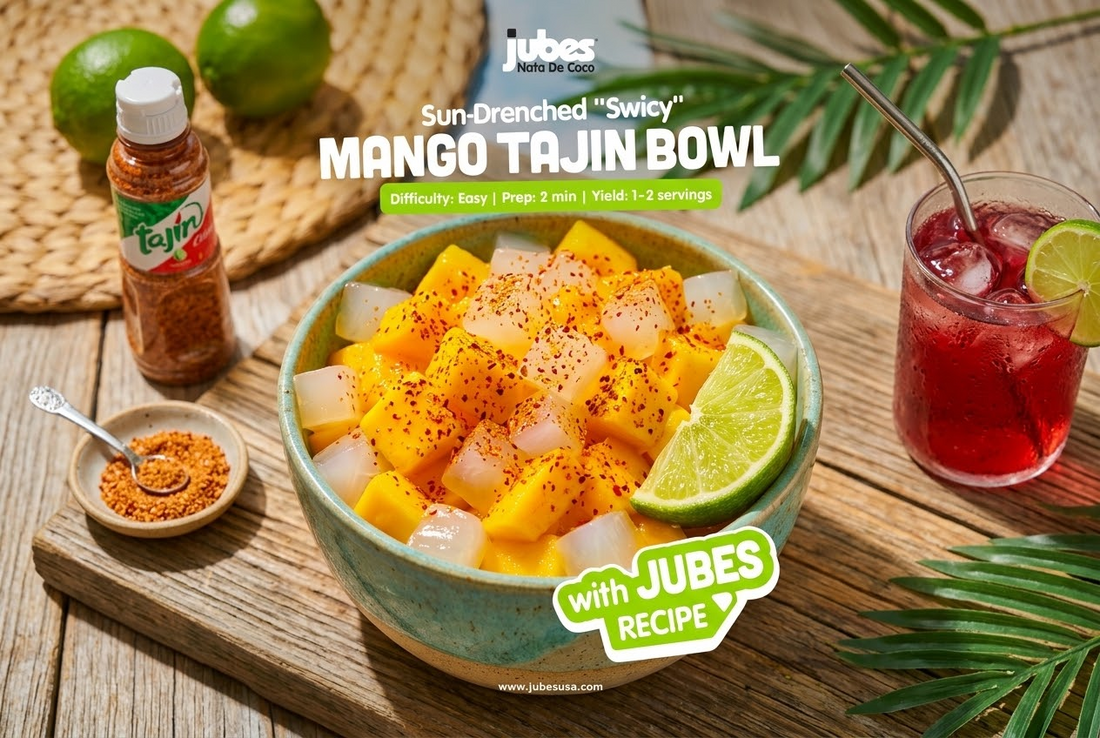 Bowl of mango and Jubes coconut jelly cubes dusted with Tajin chili-lime seasoning, lime wedge, beside a Tajin bottle and iced drink.