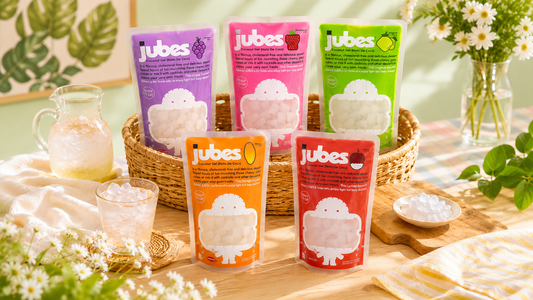 An assortment of five different flavored Jubes Nata De Coco pouches displayed on a table with an iced drink and a wicker basket.