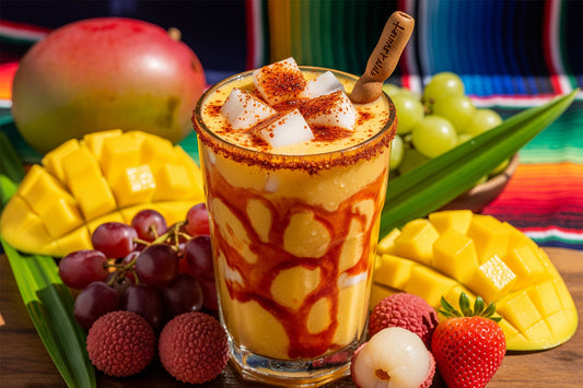 Glass of Mangonada with Jubes nata de coco cubes, chamoy, and Tajín, surrounded by fresh mango, grapes, lychee, and strawberries.